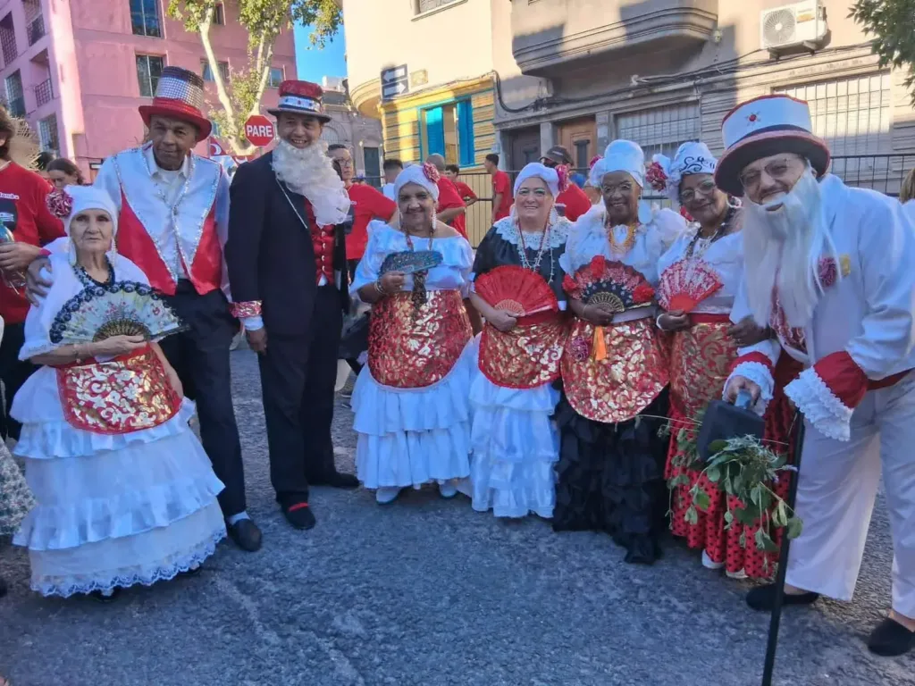 Matronas con abanicos y personajes del candombe, con vestuario blanco y rojo, en la calle.